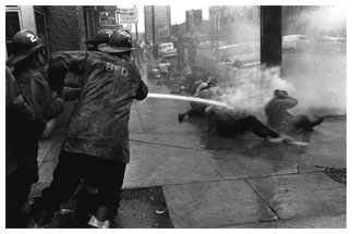 Firefighters aim a high-pressure hose at a group of protestors sitting on the pavement in Birmingham, AL.
