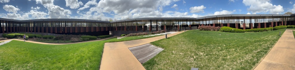 Hundreds of steel column monuments in the distance behind grass.